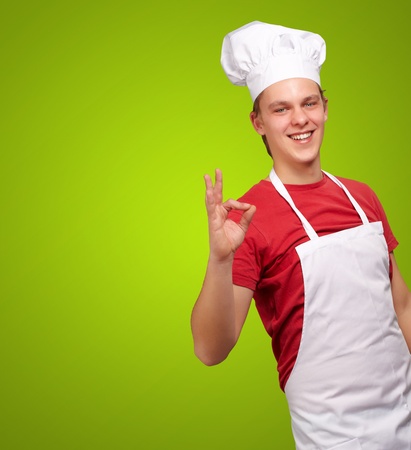 portrait of young cook man doing success symbol over green backgroundの写真素材