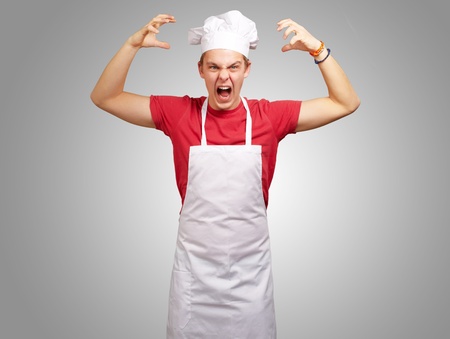 portrait of young cook man wearing apron doing aggressive gesture over greyの写真素材
