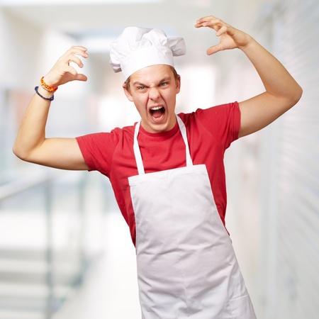 portrait of young cook man wearing apron doing aggressive gesture over abstract backgroundの写真素材