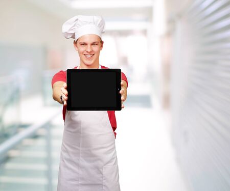 portrait of young cook man showing a digital tablet at entrance of modern buildingの写真素材
