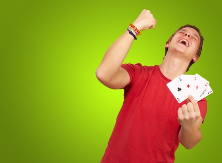 portrait of young man doing a winner gesture playing poker over green