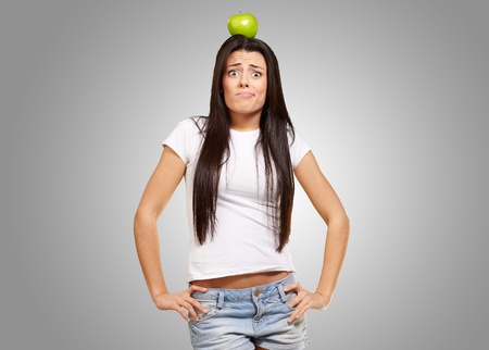 portrait of young woman holding green apple on her head over greyの写真素材