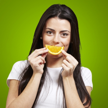 woman with an orange slice as a smile against a green backgroundの写真素材