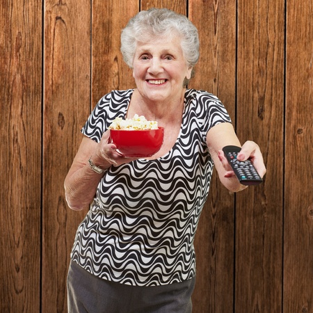 portrait of happy senior woman looking the tv against a wooden wallの写真素材