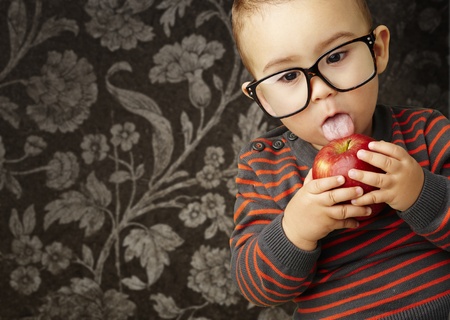 young boy licking a red apple against a vintage backgroundの写真素材