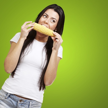 woman eating a delicious corncob against a green backgroundの写真素材
