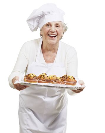 senior woman cook holding a tray with muffins against a white backgroundの写真素材