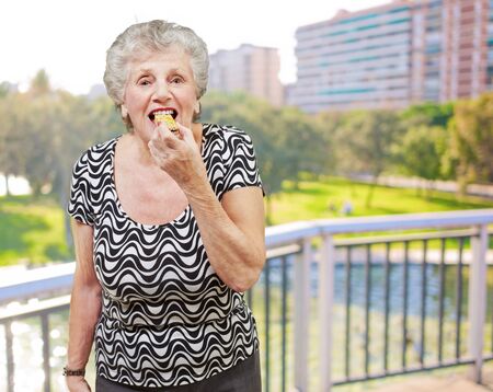 Portrait of senior woman eating a cereal bar against a parkの写真素材