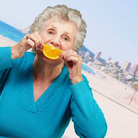 portrait of senior woman smiling and holding a orange slice in the beachの写真素材