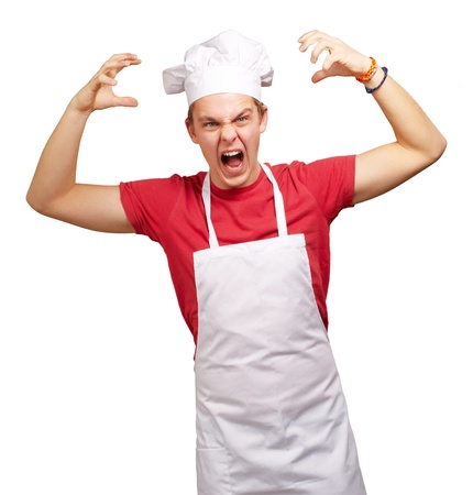 portrait of young cook man wearing apron doing aggressive gesture over whiteの写真素材