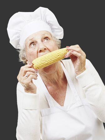 senior woman cook eating a corncob against a black backgroundの写真素材