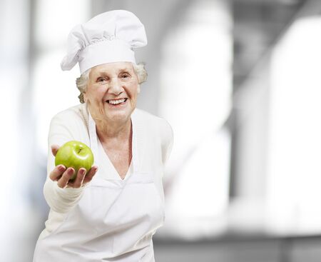 senior woman cook offering a green apple, indoorの写真素材
