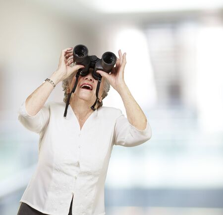 portrait of senior woman looking through a binoculars, indoorの写真素材