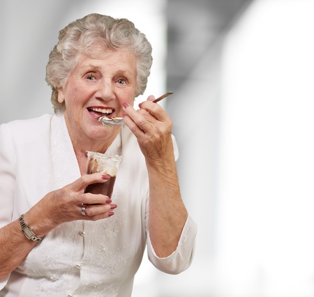 portrait of senior woman eating chocolate and cream cup indoorの写真素材