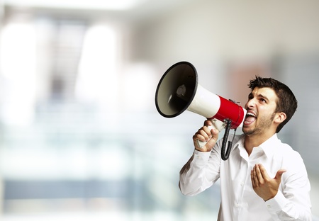 portrait of young man shouting with megaphone against a abstract backgroundの写真素材