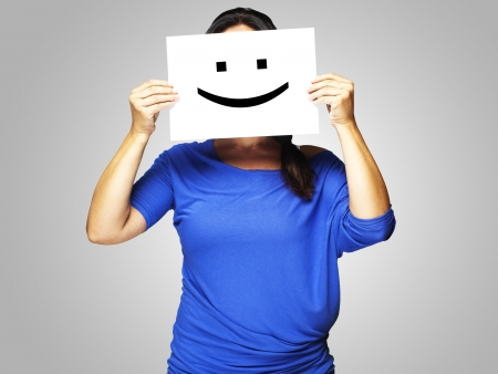 Woman showing a happy emoticon in front of face over grey backgroundの写真素材