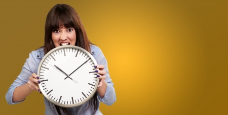 A Young Girl Holding A Clock And Angry On Yellow Backgroundの写真素材