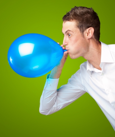 Portrait Of Young Man Blowing A Balloon Isolated On Green Backgroundの写真素材