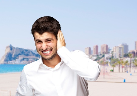 portrait of irritated young man hearing a loud against a beach