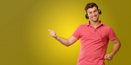 Young man wearing headphones isolated on yellow backgroundの写真素材
