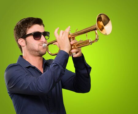 A Young Man Blowing A Trumpet On Green Backgroundの写真素材