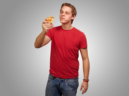 portrait of a young man eating pizza on a gray backgroundの写真素材
