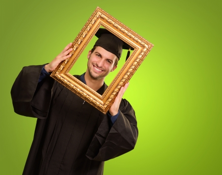 Graduate man looking through a frame on green backgroundの写真素材