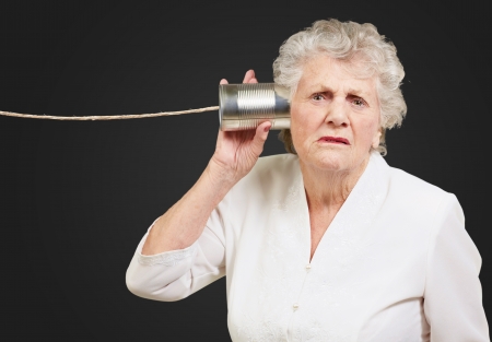 Portrait of a senior woman hearing with metal tin on black backgroundの写真素材