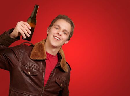portrait of young man holding beer on red background