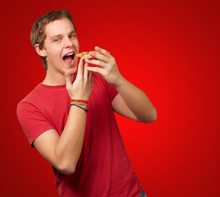 portrait of young man eating pizza over red backgroundの写真素材