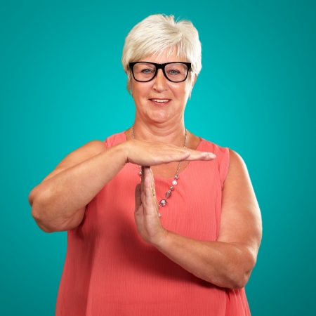 Portrait Of A Senior Woman Showing Time Out Signal On A Turquoise Backgroundの写真素材