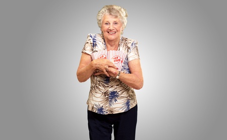 Portrait Of A Senior Woman Holding Popcorn Box On gray Backgroundの写真素材