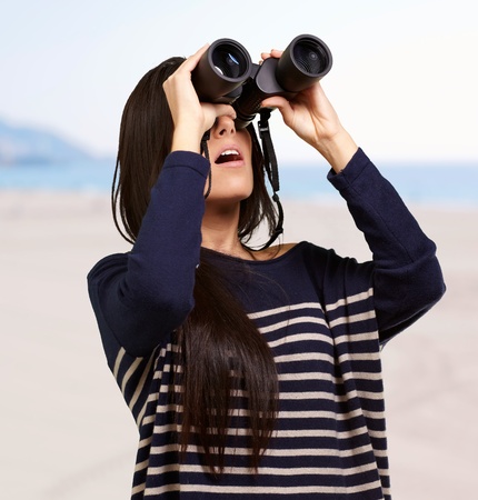 portrait of young woman looking through a binoculars against a beachの写真素材