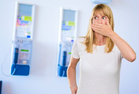 Young Woman With Hand On Mouth against a wall with two phone boxes