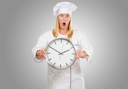 Shocked Female Chef Holding Clock against a grey backgroundの写真素材