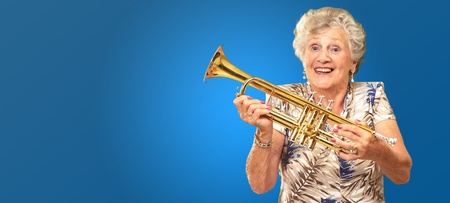 Portrait Of A Senior Woman Holding A Trumpet On Blue Backgroundの写真素材