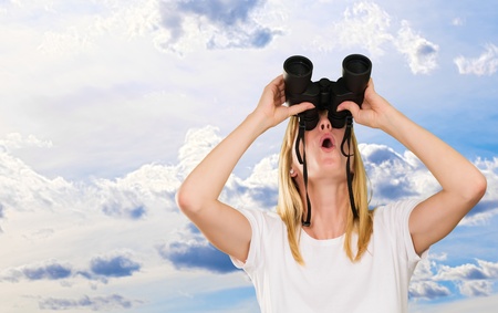 woman lookin up using binoculars against a cloudy sky backgroundの写真素材