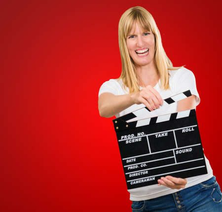 Happy Woman Holding Clapper Board against a red backgroundの写真素材