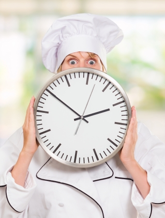 worried chef hiding behind a clock, outdoorの写真素材