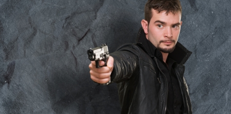 handsome man pointing with gun against a grunge backgroundの写真素材