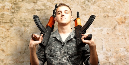 Portrait Of Soldier Holding Gun On s brown rock Background