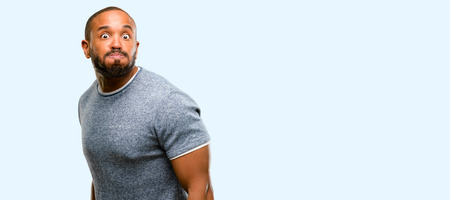 African american man with beard puffing out cheeks, having fun making funny face isolated over blue backgroundの写真素材
