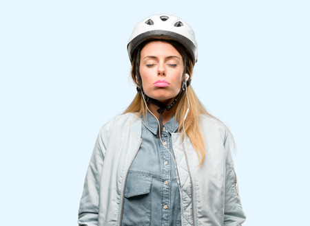 Young woman with bike helmet and earphones with sleepy expression, being overworked and tiredの写真素材