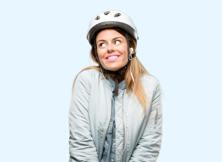 Young woman with bike helmet and earphones thinking and looking up expressing doubt and wonderの写真素材