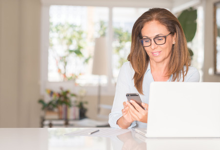 Middle age woman using smartphone and laptop, indoorの写真素材