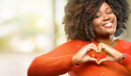 Beautiful african woman happy showing love with hands in heart shape expressing healthy and marriage symbol, outdoorの写真素材