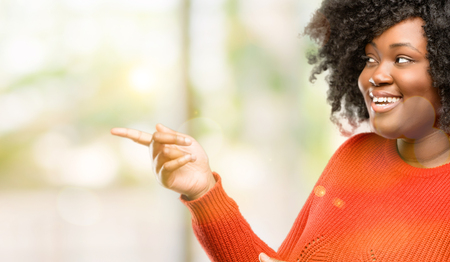 Beautiful african woman pointing away side with finger, outdoorの写真素材