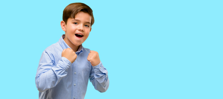 Handsome toddler child with green eyes happy and excited expressing winning gesture. Successful and celebrating victory, triumphant over blue backgroundの写真素材