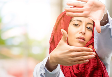 Young arab woman wearing hijab confident and happy showing hands to camera, composing and framing gestureの写真素材