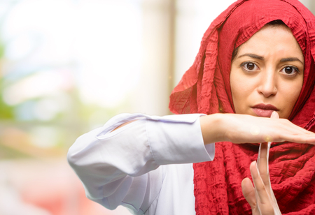 Young arab woman wearing hijab serious making a time out gesture with handsの写真素材